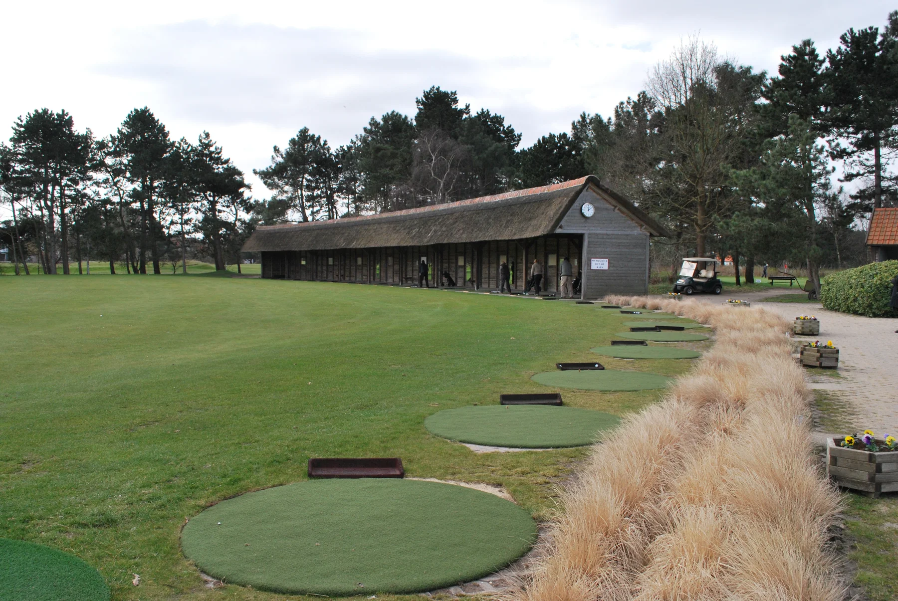 Round driving range mats under a thatched roof